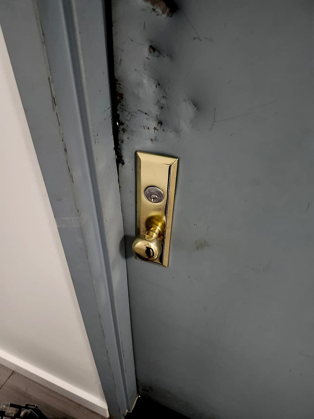 Pry marks on an apartment door and frame next to an old brass lock