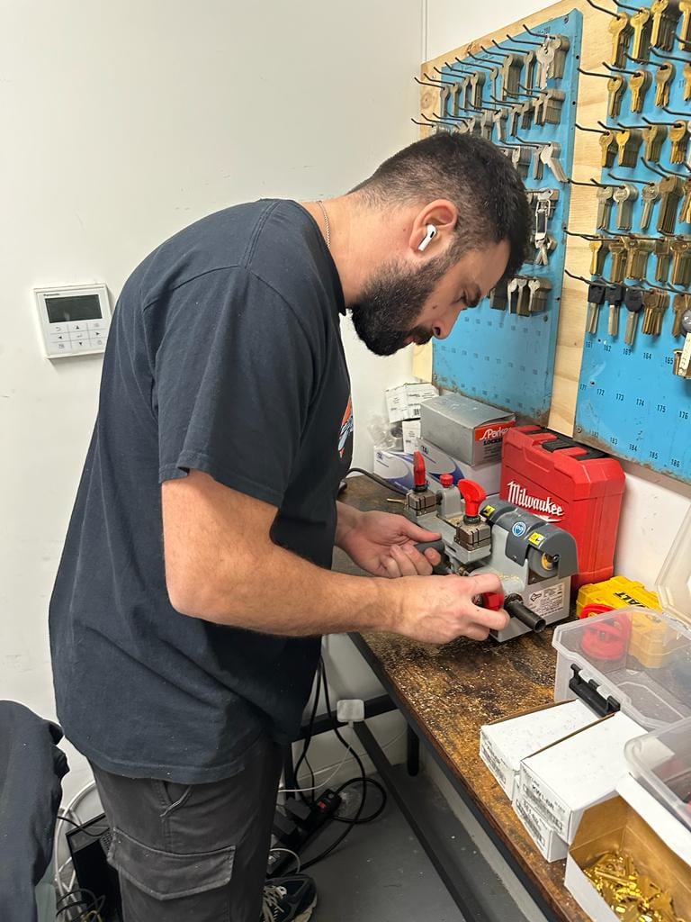 Sunny Locksmith technician cutting a car key on the shop key machine, West Village NYC