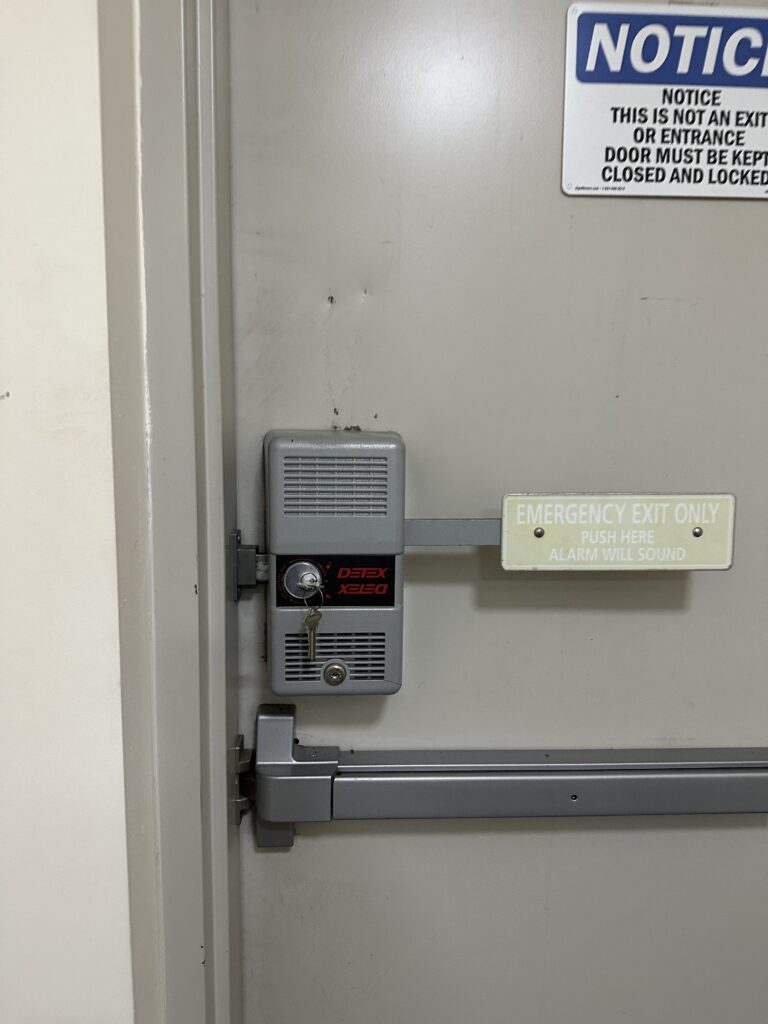 Professional installation of a heavy-duty Detex panic bar on a commercial steel door for emergency exit compliance.
